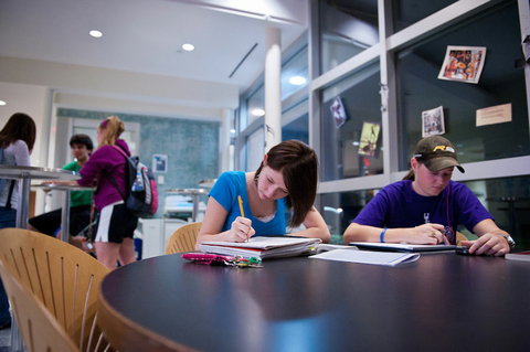 two students sitting at a table writing in their notebooks