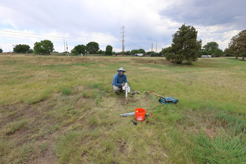 Researcher installing soil moisture and temperature sensors in a grassy field beneath a partly cloudy sky