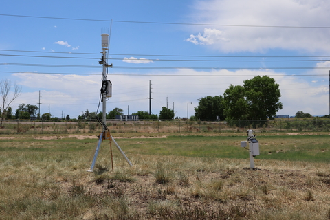 Weather monitoring station with sensors mounted on tripod in dry urban field