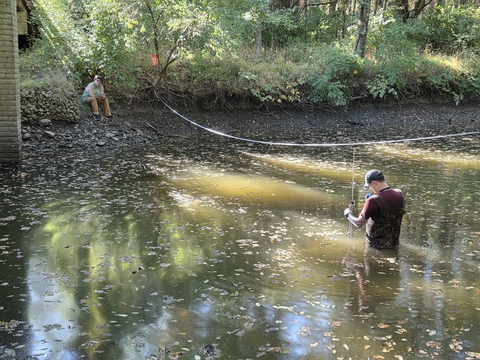 Hydrologist wading in stream collecting water measurements with measuring tape across channel