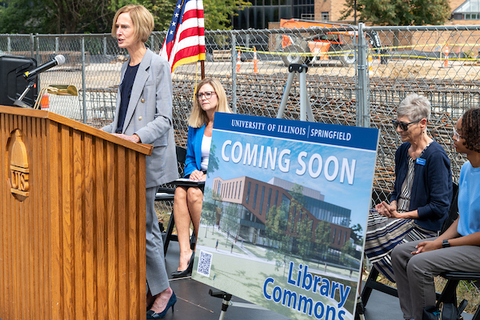 Chancellor Gooch speaking at a podium next to a sign for the new Library Commons which is under construction.