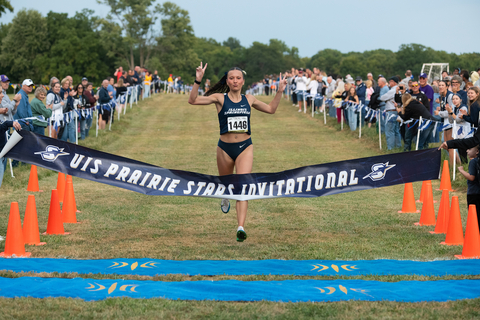 UIS cross country runner crosses the finish line at the Prairie Stars Invitational as spectators cheer.