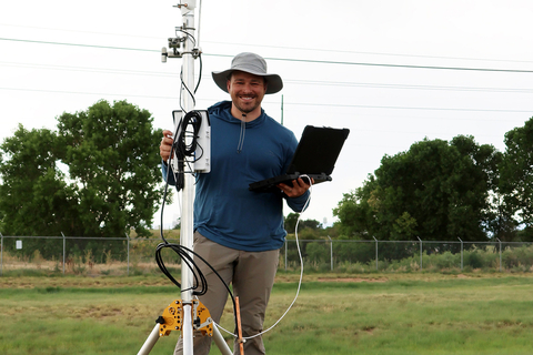 UIS researcher stands outdoors holding monitoring equipment and a laptop during field data collection.