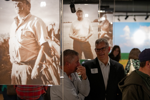 Visitors talk inside a museum gallery featuring large historic farm photography displays.