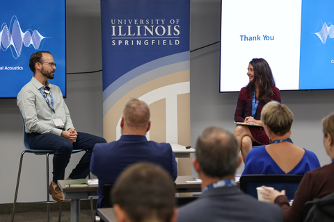 UIS speaker and moderator sit on stage during a campus event with an audience listening.