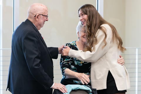 Three people smiling and embracing warmly indoors.