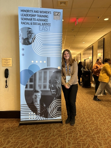 UIS teacher education student standing next to a banner at the Minority and Women's Leadership Training Seminar to Advance Racial and Social Justice.