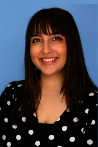 Smiling woman with straight hair and polka dot blouse, blue background.