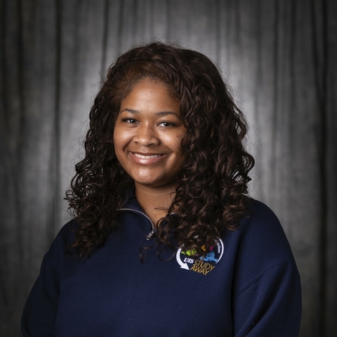 Student with brown curly hair smiling wearing a blue sweatshirt