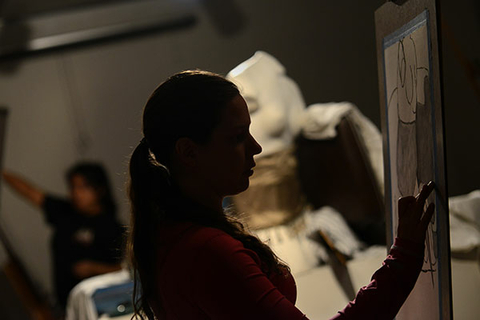 Silhouette of a person drawing on a tablet in a dimly lit room.