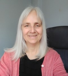 Smiling woman with long gray hair in a red cardigan.