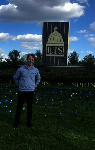 Christopher posing for a picture in front of the UIS sign.