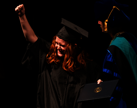 A person in cap and gown fist pumping.
