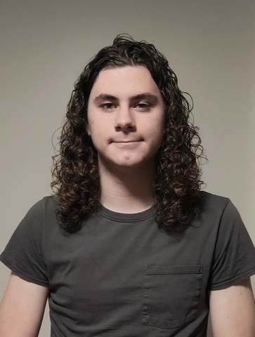 student posed in front of a beige background with dark gray shirt.