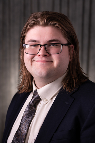 student posed in front of dark gray background with shirt, tie and a black suit jacket.