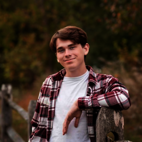 student posed in front of a fence with a white t-shirt and plaid button up.