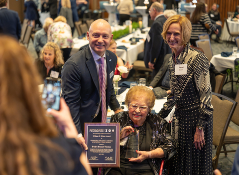 Group posing with award at a formal event, woman seated holding plaque.