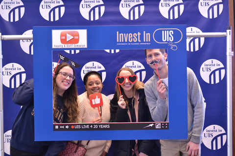 Colleagues looking through photo frame with props to celebrate investing in UIS.