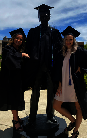 Two graduates smiling with the Lincoln statue.