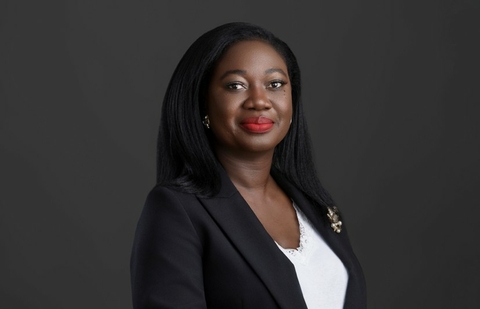 Smiling woman in a black blazer on a dark background.