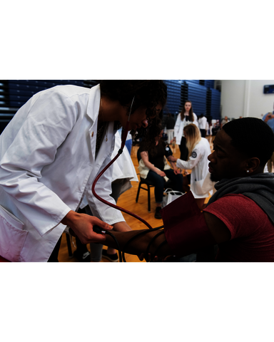 a female doctor taking the blood pressure of a male student