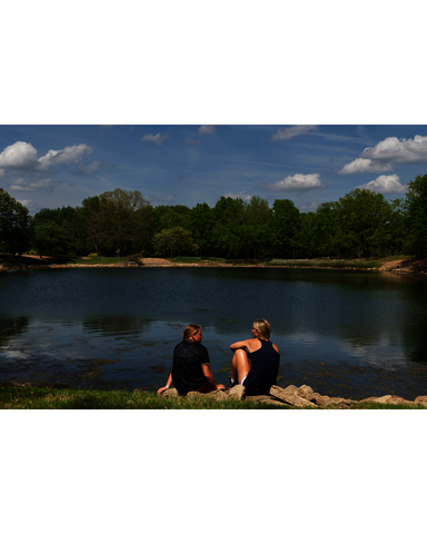 two female students sitting by a small lake near campus