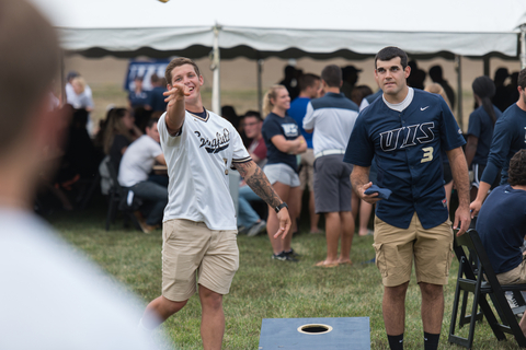 Two men playing cornhole at an outdoor gathering.