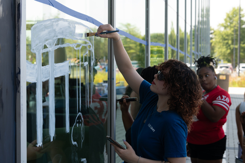 Person painting on a window with a brush, others watching.