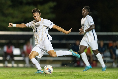Soccer player kicks ball during a night game, teammate in the background.