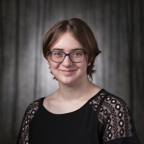 Smiling photo of a female student with a pixie cut brown hair and black rimmed glasses