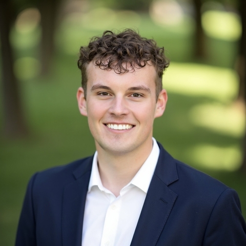 student posed in front of a green background with a white button down and navy blue suit jacket