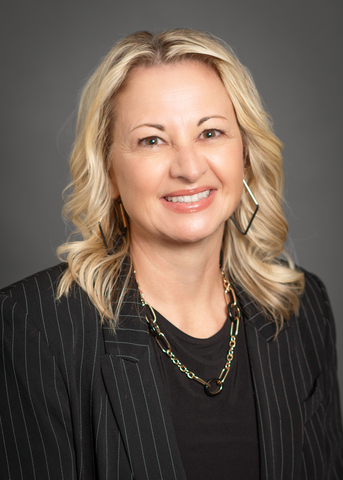Professional headshot of Angela Nguyen smiling against a gray background, wearing a black pinstriped blazer and gold jewelry.