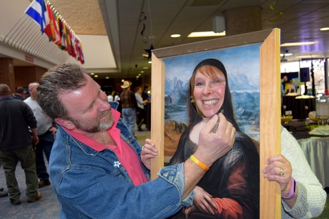 A man pretending to paint a picture with a cut-out featuring a woman's face.