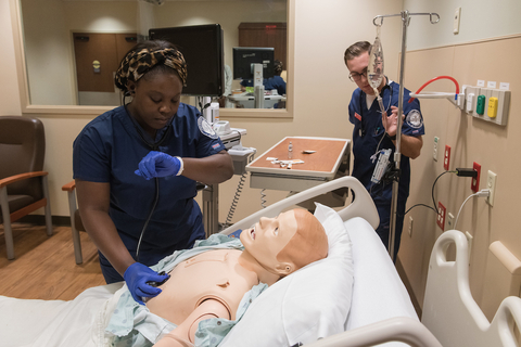 Two nursing students learning how to check vital signs on a simulator.