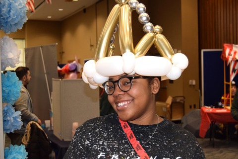 A woman wearing a hat made out of gold, white and silver balloons. 
