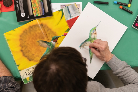 elderly woman drawing a hummingbird from a photo reference