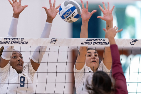 Two volleyball players trying to hit a ball coming over the net.