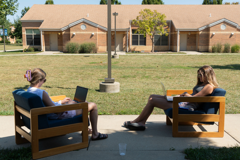two students sitting outside their townhouse on their laptops
