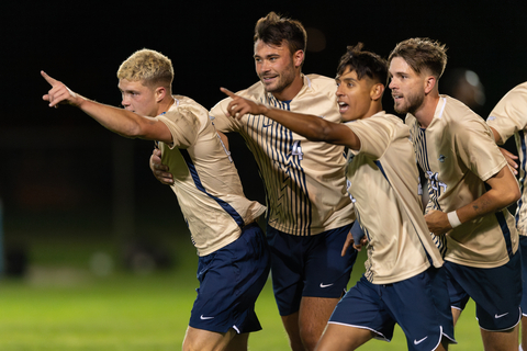 A group of four men's soccer players smiling and pointing.