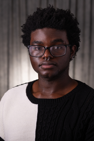 Professional headshot of Deme wearing a white and black sweater, smiling with a neutral background.