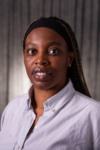 Professional headshot of Enimien wearing a stripped button-down shirt, smiling with a neutral background.