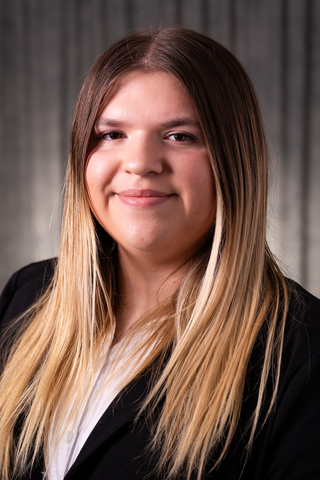 Professional headshot of Gabby wearing a white button-down shirt and black blazer, smiling with a neutral background.