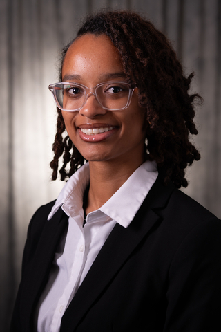 Professional headshot of Jazel wearing a white button-down shirt and black blazer, smiling with a neutral background.