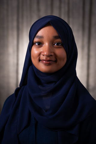 Professional headshot of Minnah wearing a blue hijab, smiling with a neutral background.