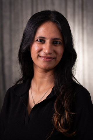 Professional headshot of Shrushti wearing a black button-down shirt, smiling with a neutral background.