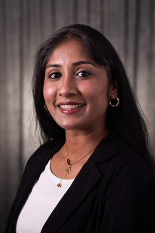 Professional headshot of Vidharthi wearing a white shirt and black blazer, smiling with a neutral background.