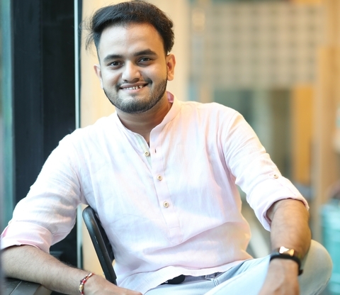 Ajay Jayshree, a picture of a smiling seated man in a light pink shirt