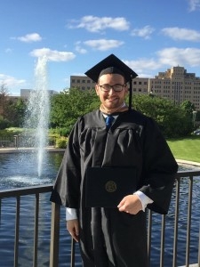 a graduate in a cap and gown posing in front of a fountain