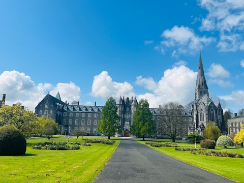 University of Maynooth in Ireland. Paved road with green grass on both sides leading up to a gray castle-like university building