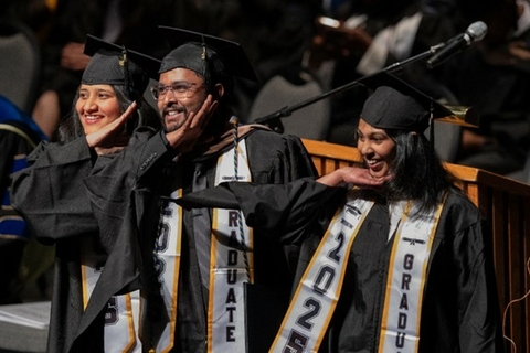 Three students posing on stage at graduation.